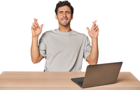 Hispanic young man working on laptop crossing fingers for having luck - Powered by Adobe