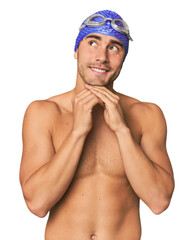 Young Hispanic man with swim gear keeps hands under chin, is looking happily aside.