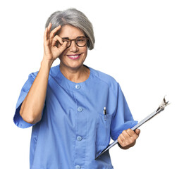 Caucasian mid-age nurse holding report excited keeping ok gesture on eye.