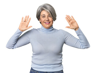Caucasian mid-age female on studio background showing number ten with hands.