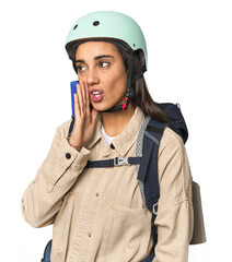 Hispanic young woman with mountain gear is saying a secret hot braking news and looking aside