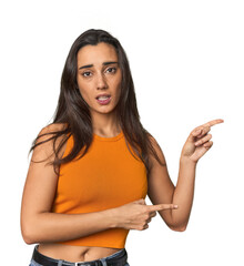 Hispanic young woman shocked pointing with index fingers to a copy space.