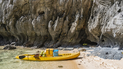 A bright yellow canoe is moored to the shore. Coconuts are stacked on the boat, there are...