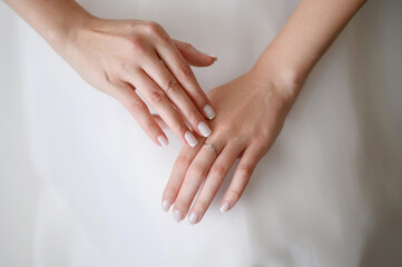 Beautiful gentle hands of bride with neat manicure in white wedding dress with wedding ring on her...