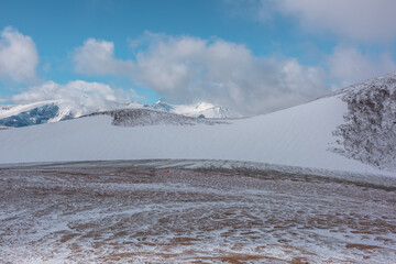 Orange tent on snowy stony pass near wide glacier and large mountain range with snow-white peak...