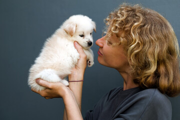 Portrait of a girl with a puppy, a woman of European appearance with curly hair holds a cute white puppy in her arms.