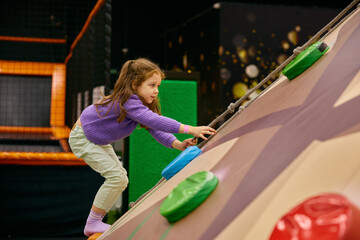 Playful excited girl child climbing rock at indoor playground