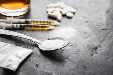 Narcotic substances in spoon, dope powder, syringes with drugs dose, white pills and glass of alcohol drink on dark textured background. Concept of addiction and bad habits