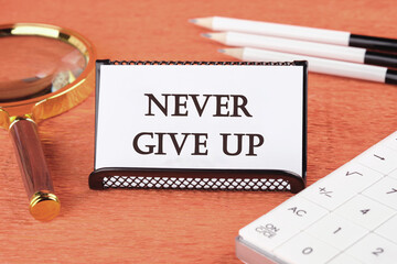 Never give up words there is a magnifying glass, a calculator, and pencils on a white business card next to it