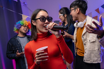 Happy asian diverse group friends singing together on party with neon light. Home party friends...