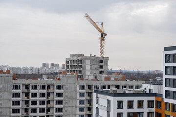 A crane and a building under construction against a blue sky background. Builders work on large...