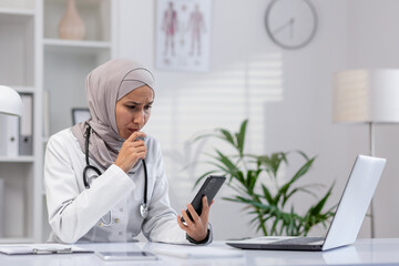A professional Muslim female doctor, wearing a hijab, looks worried as she examines patient data on...