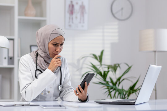 A professional Muslim female doctor, wearing a hijab, looks worried as she examines patient data on her smartphone in a modern clinic office. - Powered by Adobe