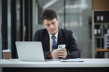 Businessman with smartphone and laptop and analyzing a chart  while working in the office, Business and financial concept.