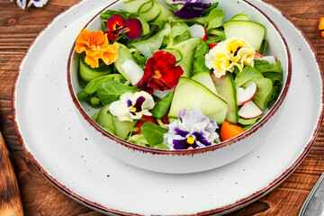 Salad of vegetables and flowers on wooden background.