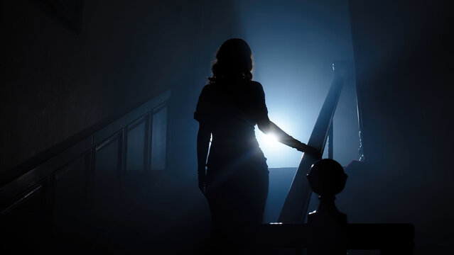 Beauty and form. The silhouette of a beautiful, young woman against a dark background is climbing up the old stairs. - Powered by Adobe