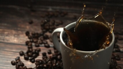 Falling drop in hot espresso in coffee cup decorated with piles of coffee bean placed on wooden...