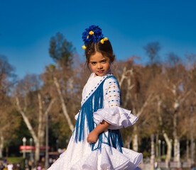 a little girl dancing flamenco dressed in a white dress with ruffles and blue fringes in a famous...