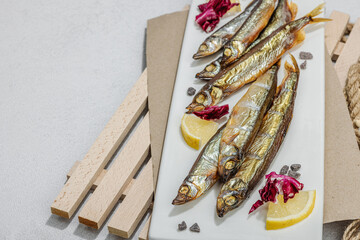 Smoked smelt with fresh lemon and herbs. Salted fish with marine decor. Trendy dish, sea rope