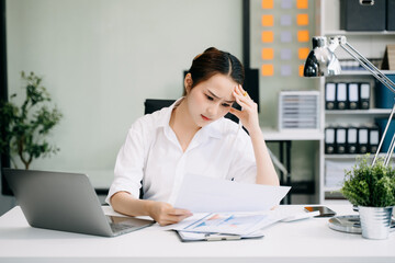 Asian woman feeling migraine head strain.Overworked businesswoman financier while working on laptop...