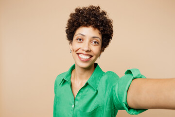 Close up young woman of African American ethnicity wear green shirt casual clothes doing selfie shot pov on mobile cell phone isolated on plain pastel light beige background studio. Lifestyle concept.