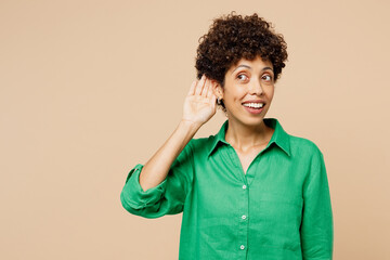 Young curious nosy woman of African American ethnicity wear green shirt casual clothes try to hear you overhear listening intently isolated on plain pastel beige background studio. Lifestyle concept. - obrazy, fototapety, plakaty