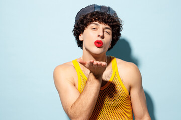 Young happy gay Latin man wear mesh tank top hat clothes with red lipstick make up blow send air...