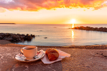 cup of coffee or tea with croissant on a morning embarkment beach with blue sea and beautiful...