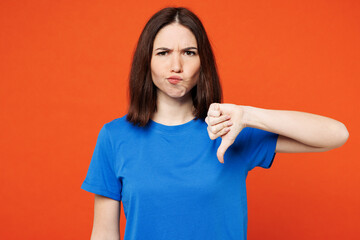 Young sad dissatisfied displeased woman wear blue t-shirt casual clothes showing thumb down dislike gesture looking camera isolated on plain red orange background studio portrait. Lifestyle concept.