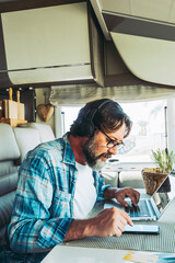 One handsome mid age man working on mobile cell phone and laptop computer inside a camper van...