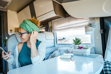 Happy modern traveler woman using phone connection inside a camper van motorhome alone. Female...