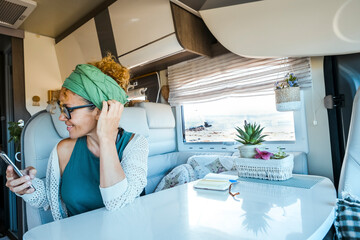 Happy modern traveler woman using phone connection inside a camper van motorhome alone. Female adult travel with renting rv vehicle for summer holiday vacation. Living full time in a motor home rv © simona