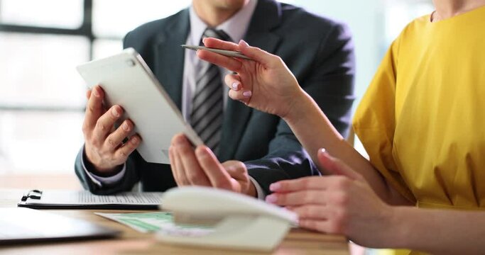 Female manager explains project tasks to man colleague with gadget pointing pen. Woman worker gives instructions to young employee at workplace slow motion