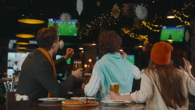 Happy excited group of friends watching football match on tv in pub