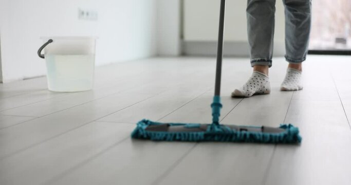 Woman cleans floor with mop in modern office at end of working day. Female in cotton socks supports workplace hygiene. Wet cleaning of dust and dirt