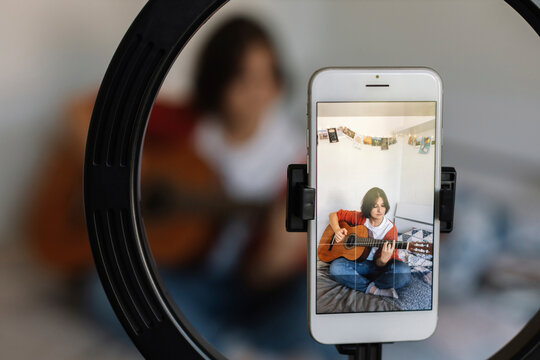 Young woman filming herself practicing guitar at home