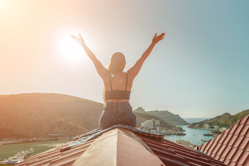 Woman sits on rooftop with outstretched arms, enjoys town view and sea mountains. Peaceful rooftop...