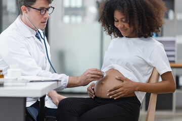 Fototapeta premium Male doctor examining a pregnant African American woman at the hospital.