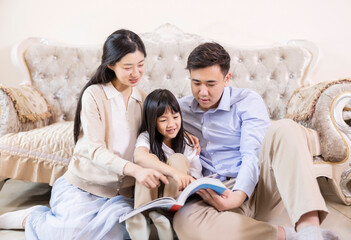 A family of three in the living room with their daughter reading and playing