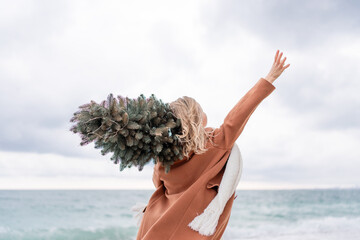 Blond woman Christmas tree sea. Christmas portrait of a happy woman walking along the beach and...