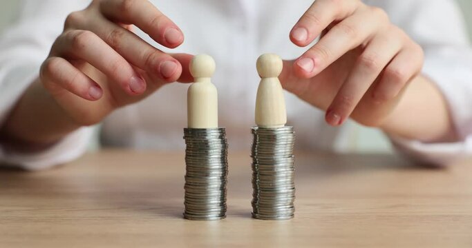 Woman puts wooden figurines on silver coins stacks on wooden desk. Equal access to money assets for business partners concept slow motion