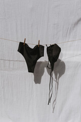 Black female swimwear hanging over white cotton cloth with strong shadows. Sunbathing on a summer...