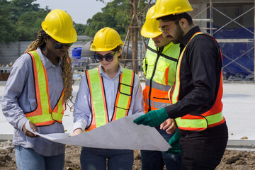 Group of construction workers gathered at a construction site reviewing some plan. Unfinished building, piles of construction material, and a partially constructed structure are in the background