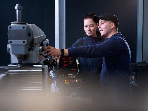 Smiling engineer explaining CNC machine to trainee at factory