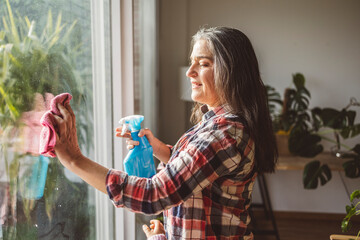 Mature woman cleaning window glass with rag at home