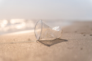 Plastic pollution and environmental problem concept. Close up of used plastic cup on the beach....
