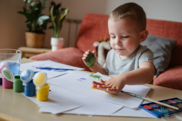 Boy making colored handprint on sheet of paper at home