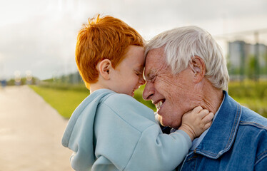 Happy senior man having fun with redhead grandson at park