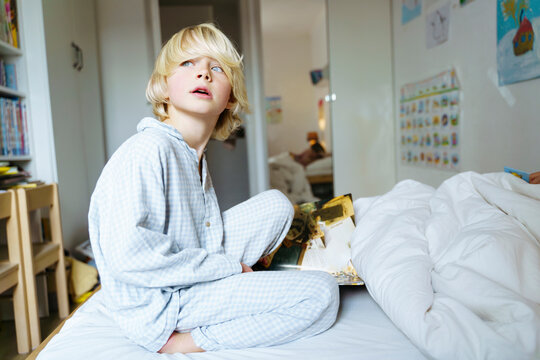Thoughtful blond boy sitting on bed at home