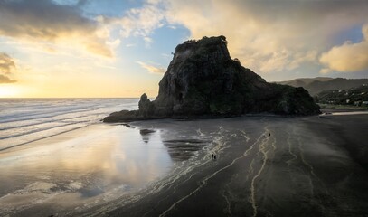 beautiful sunset and reflection of cliff on a beach in an outgoing tide. Piha, Auckland, New Zealand.